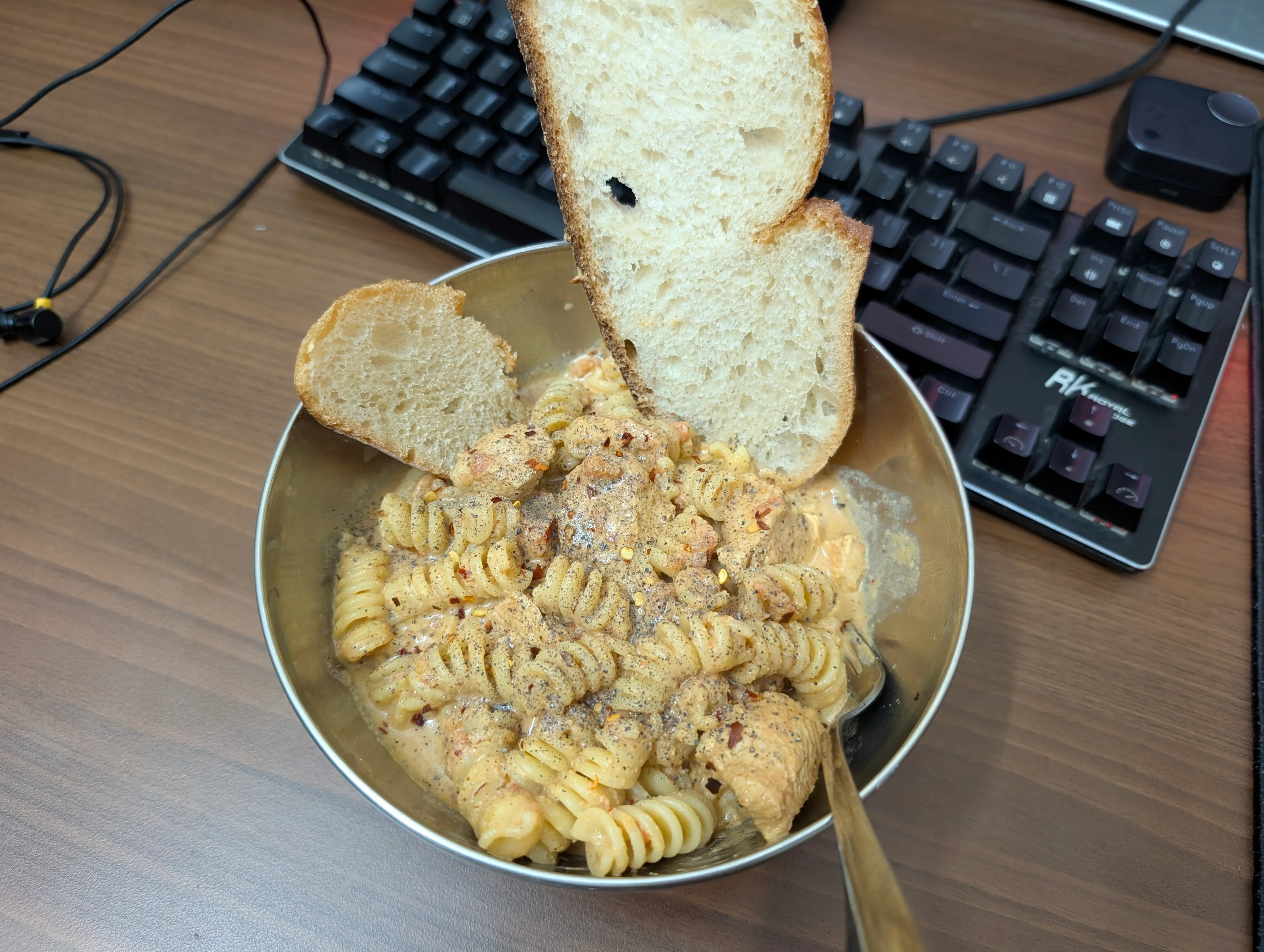 A bowl of Fusilli pasta in a creamy and tomato rich sauce with some chicken pieces and a couple of slices of sourdough bread poking out from it.