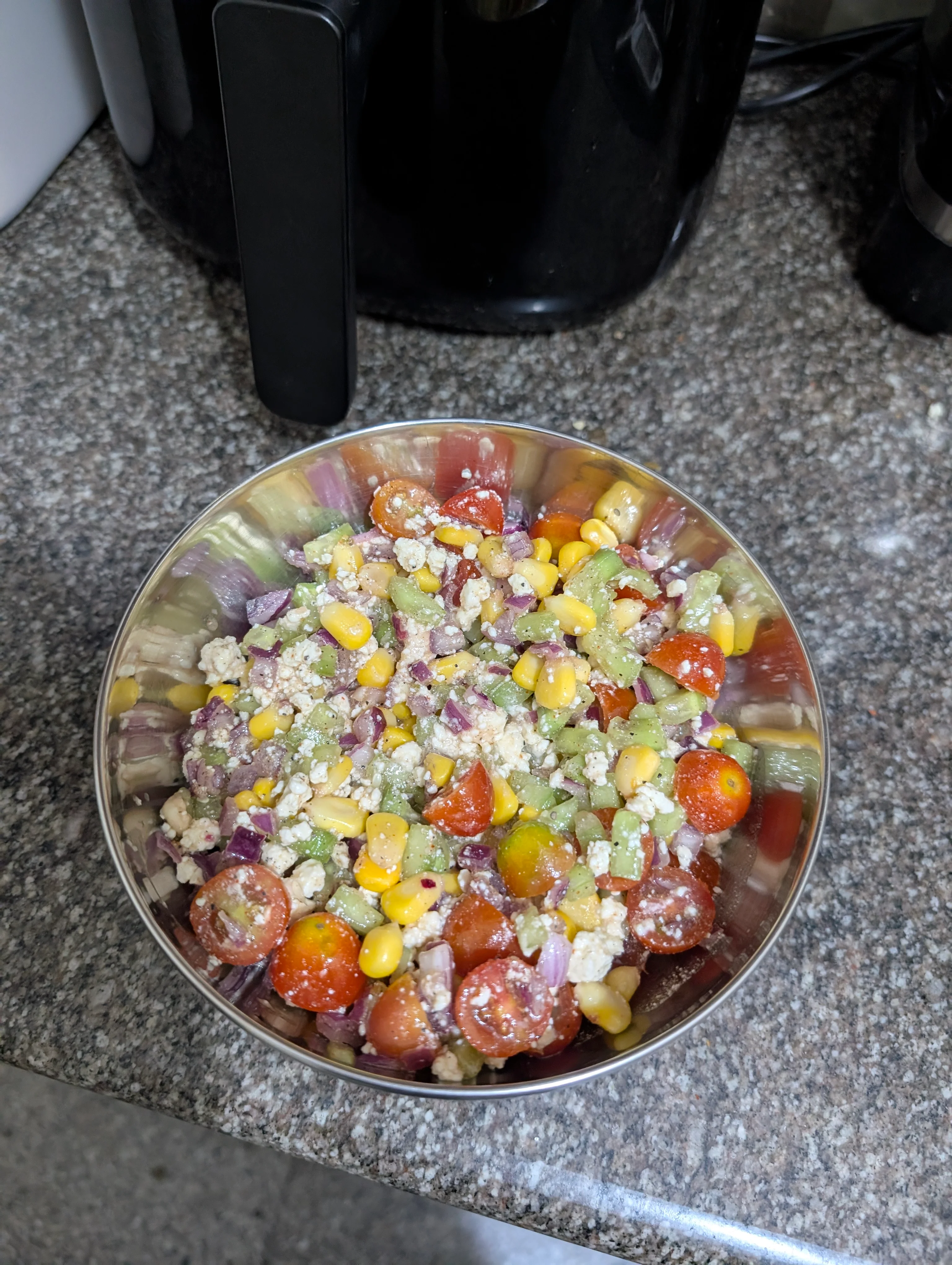 The cowboy caviar salad containing diced onions, cucumbers, cherry tomatoes, corn, feta cheese and a simple sauce made with olive oil, apple cider vinegar, lemon juice and onion powder.