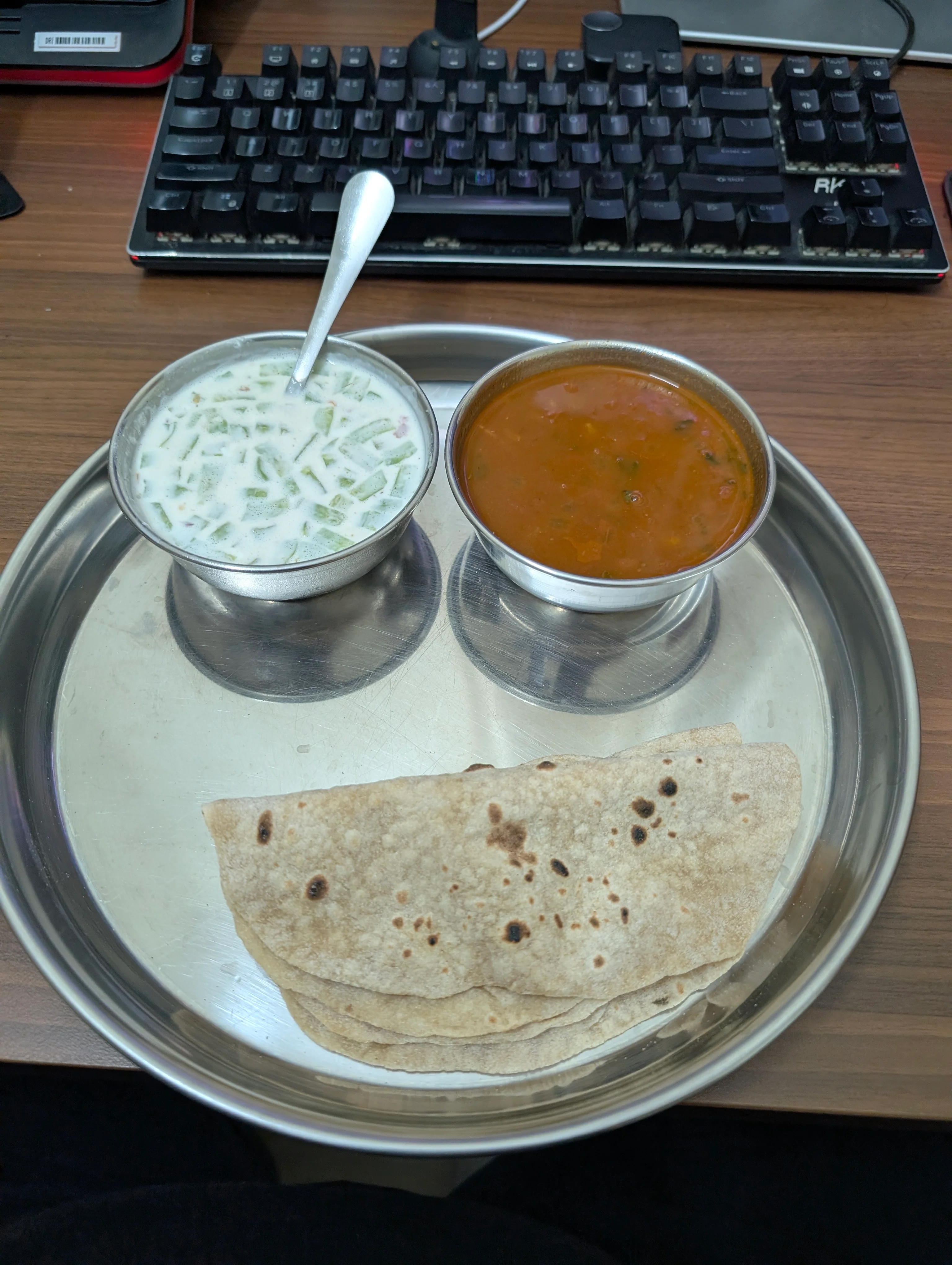 A plate with a bowl of raita, a bowl of rajma gravy and two chapattis.