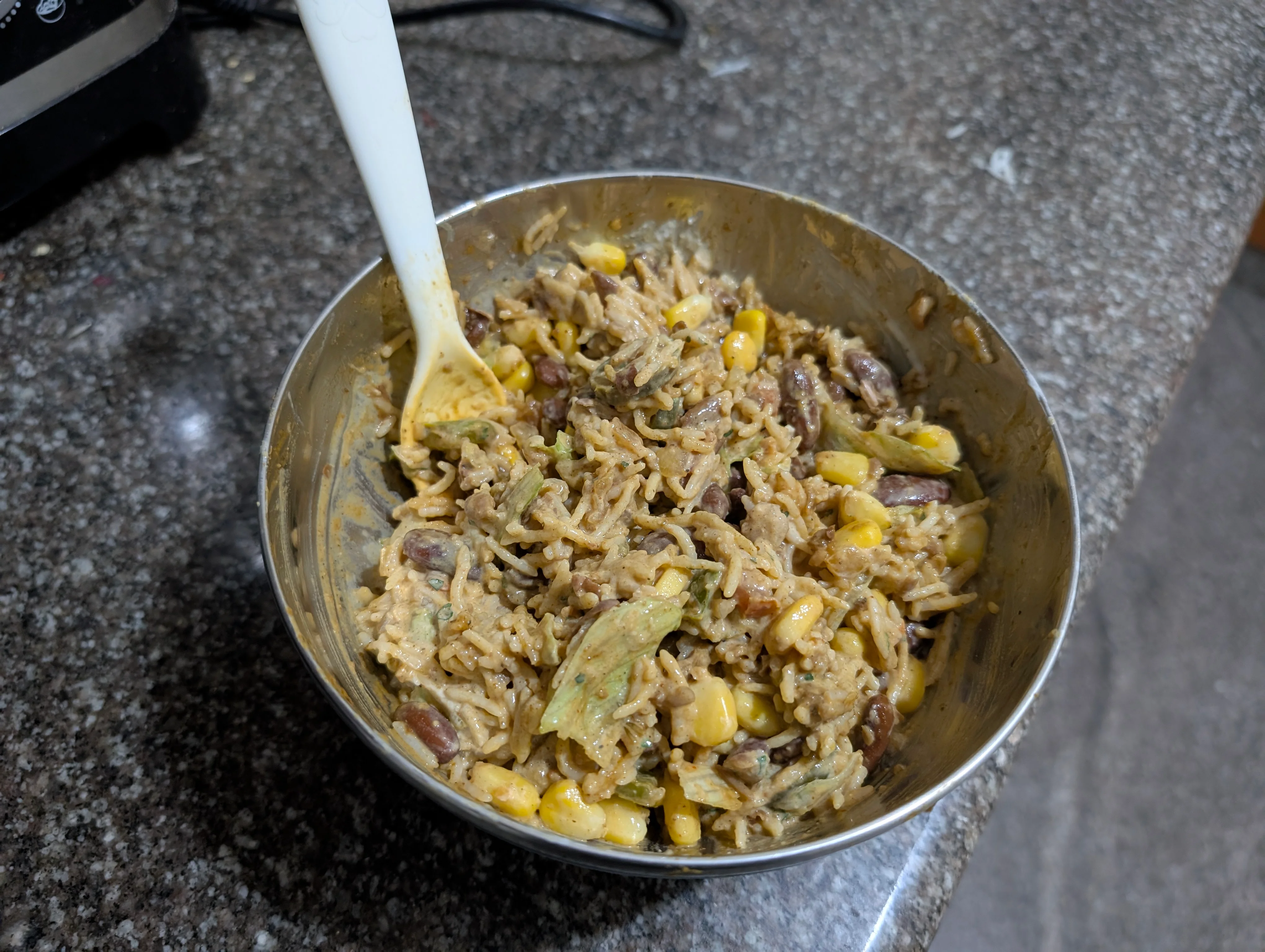 A typical burrito bowl with rice, corn, lettuce, beans, diced jalapenos and some condiments.